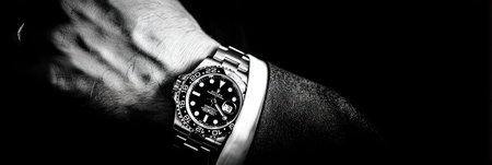 A grayscale image shows a wristwatch on a person's wrist. The watch features a dark face and a metallic band. The composition emphasizes the watch's details, set against a dark background. This image could be used for advertisements, fashion editorials, or content related to accessories and luxury items.の素材