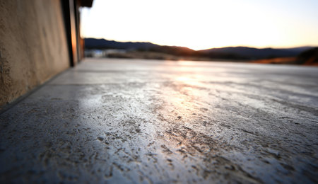 A close-up view presents a textured concrete surface under soft lighting. The image emphasizes the rough surface and subtle color variations. The background is softly blurred, likely taken outdoors during a sunset. This imagery could be useful for projects related to design, backgrounds, or textures.の素材