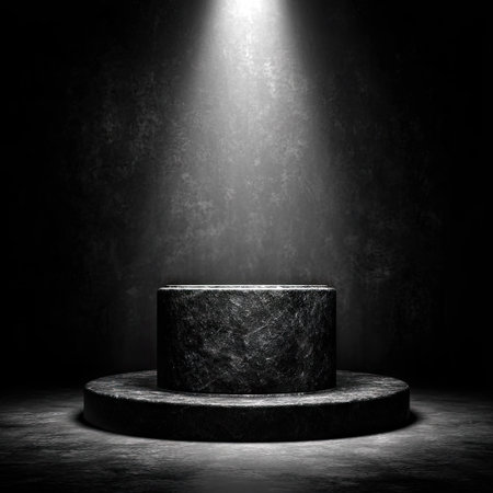 A dark, textured cylindrical podium sits on a circular base, bathed in a bright spotlight. The background is a contrasting gradient of darker tones, creating depth. The image displays a strong contrast and highlights the product area, suitable for various promotional or editorial applications.の素材