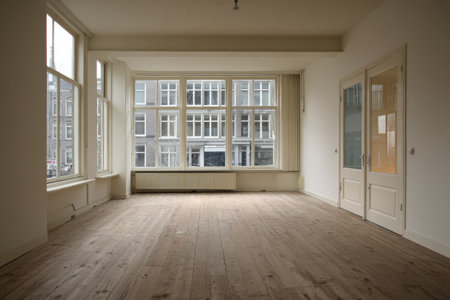 An empty interior space bathed in natural light features a wooden floor and large windows. The neutral color palette and simple lines create a sense of openness. This room's minimalist design suggests versatility for various applications, including real estate or lifestyle content. The overhead lighting adds visual interest.の素材