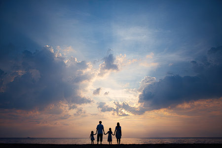 A family stands silhouetted against a dramatic sunset. The composition emphasizes a strong contrast between dark figures and the bright, colorful sky. The warm tones of the sun are complemented by the dark outlines of people. This image could be used for various commercial or editorial purposes.の素材