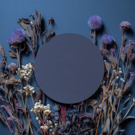 An overhead shot features a floral arrangement surrounding a dark circle. The composition includes dried flowers in shades of purple, brown, and white against a deep blue backdrop. This image could be utilized for various creative projects such as decorative designs and print media.の素材