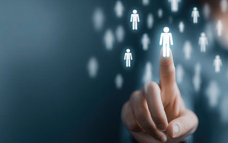A hand touches a glowing human figure icon, set against a dark blue background. The composition uses soft focus and shallow depth of field, with light illuminating the digital icons. This image could be used in a variety of visual communication projects for business or advertising.の素材
