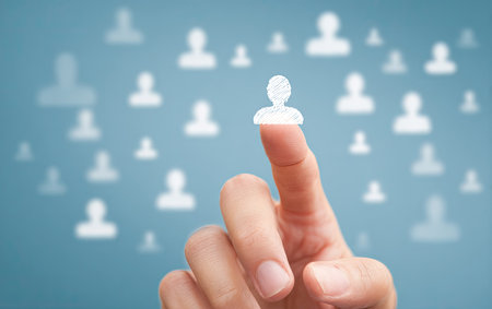 A hand with skin tones points towards a glowing human icon surrounded by other similar symbols. The background is a soft blue with blurred icons. The composition utilizes shallow depth of field, with soft lighting and focus on the hand. This image is suitable for various commercial uses, including technology, business, and social networking themes.の素材