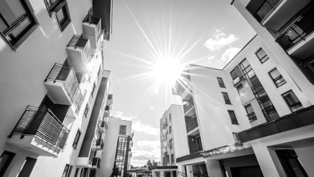 An upward perspective captures modern residential buildings under a radiant sun, presented in grayscale. The clean lines of the architecture contrast with the bright sky, creating a stark visual. This image could be used for architectural concepts or to represent property development, suitable for a range of editorial and commercial applications.の素材