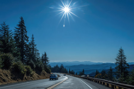 A scenic road winds through a mountain range under a clear, bright blue sky. The composition features a long asphalt road and several cars. The natural environment is illuminated by bright sunlight creating a sense of travel and adventure. This imagery might be suitable for promotional materials or editorial content.の素材