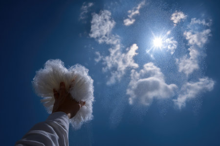 Woman's hand in white fluffy hat against the blue sky with cloudsの素材