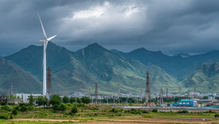Wind turbine in the middle of the meadow with mountains and cloudy skyの素材