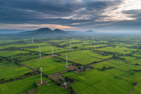 Aerial view of wind turbines in paddy field with mountain backgroundの素材
