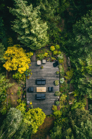 An overhead view reveals a wooden deck nestled within a lush forest environment, featuring an arrangement of seating and a table. The scene showcases a palette of greens and yellows. This image could be used for illustrating outdoor living, architectural design, or nature-related content. It is suitable for commercial and editorial use.の素材