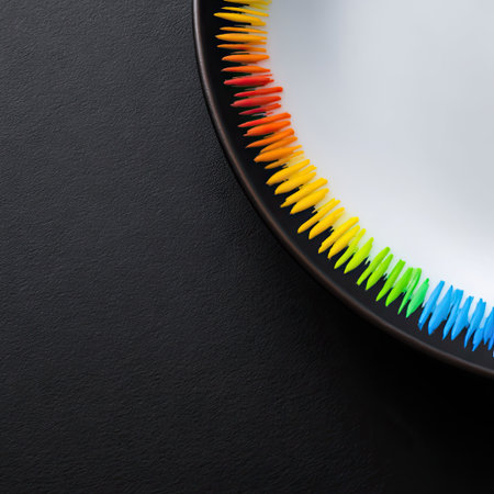 An abstract composition features a rainbow-colored spring coiled around a dark circular element. The visual highlights a gradient of colors including red, orange, yellow, green, and blue. The design appears against a black backdrop, offering a contrast and providing a space for various creative applications.の素材