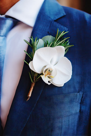 A close-up captures a white orchid boutonniere on a blue blazer. The composition highlights the flower's delicate petals and the texture of the fabric. The image features natural lighting with a shallow depth of field, offering potential uses in editorial, wedding, or fashion related projects.の素材