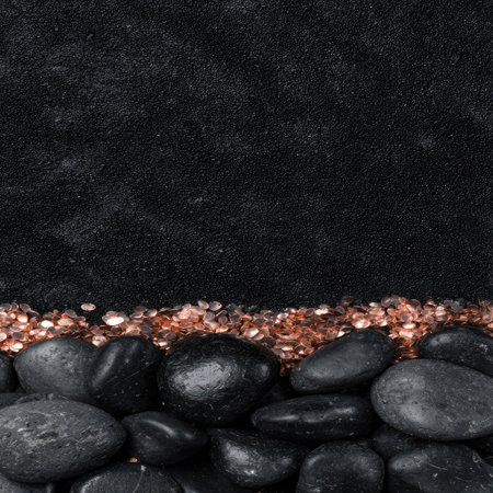 This image showcases a collection of smooth, black stones in the foreground. They rest against a backdrop of a rough, dark surface. Scattered tiny, copper-colored particles add visual interest. The composition suggests a natural environment or decorative setting, suitable for various design projects.の素材