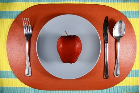a photo of a red apple on a plate with spoon fork and knifeの素材