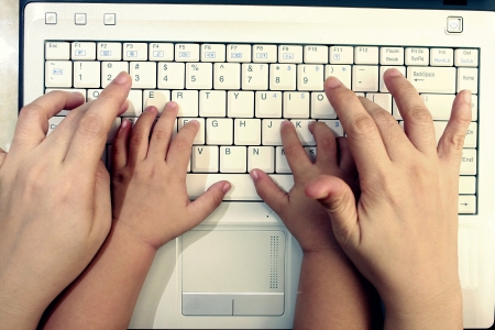 hands of parents or teacher or adult guiding or teaching a student to type on a computer or laptopの素材