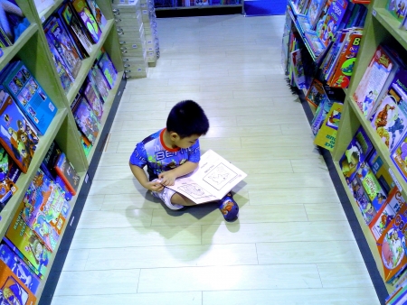Little asian boy reading childrens books in a bookstoreの素材
