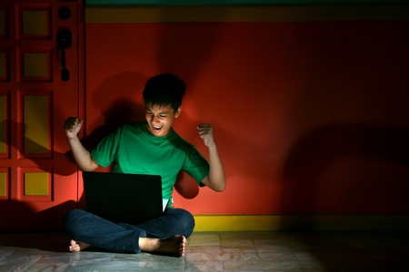 Young asian teen with a laptop computer and excited, sitted in an empty living roomの素材