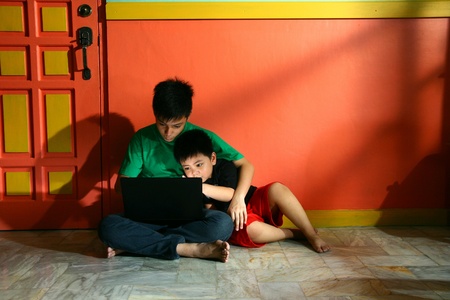 Young asian children, siblings or brothers with a laptop computer, sitted in an empty living roomの素材