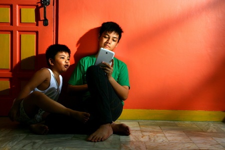 Young asian boys, brothers playing with a tablet in a living roomの素材
