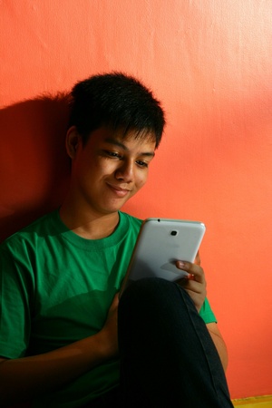 Young asian teen playing with a tablet in a living roomの素材