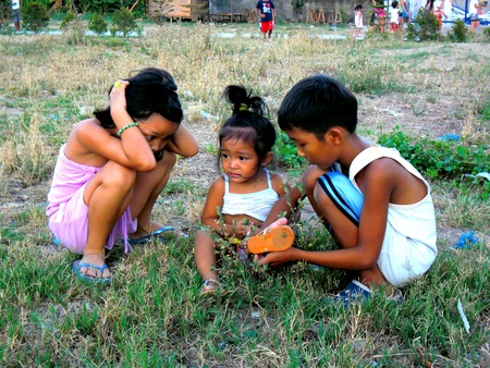 Asian children sitting on the ground in a grass fieldの素材