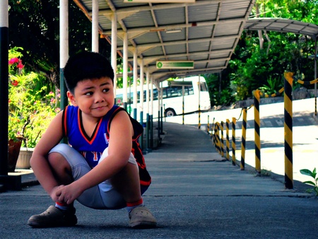 Asian kid resting under the shade of a covered hallwayの素材