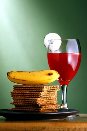 Stack or pile of crackers, a banana and a goblet of fruit juice with cucumber slicesの素材