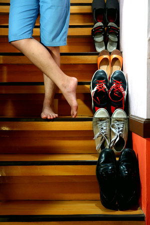 Person on barefeet and cross legged standing beside Different shoes on a staircase
