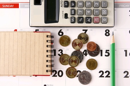 Coins, pencil, notebook, calendar and calculator on a tableの素材