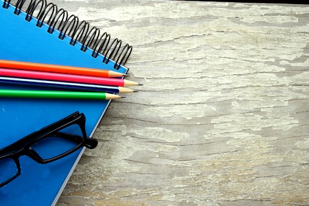 Colored pencils, eyeglasses and a notebook on a wooden tableの素材