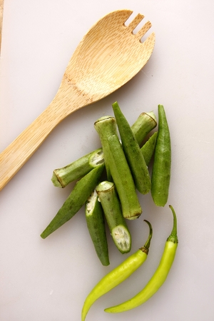 Sliced okra green chili and a wooden spoon on a white chopping boardの写真素材