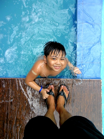 Young boy in a swimming pool and the feet of his parentの写真素材