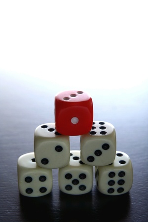 One Red game dice on top of several white game diceの素材