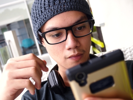 Teenager wearing a bonnet and eyeglasses using a smartphoneの写真素材