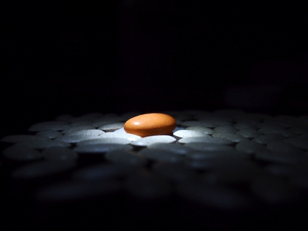 Lone orange colored pill among a bunch of white pillsの写真素材