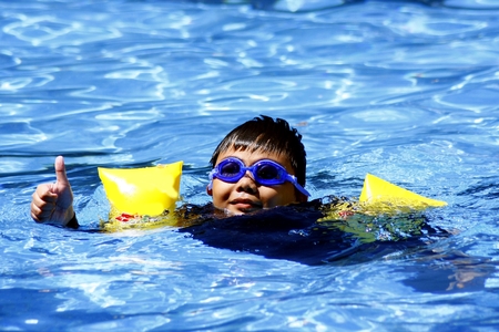 Young kid giving the thumbs up sign while swimming in a swimming pool.の写真素材