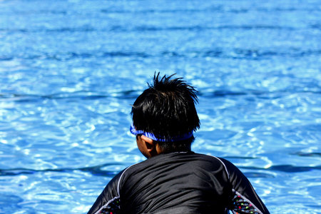 Young kid sitting by the edge of a swimming pool.