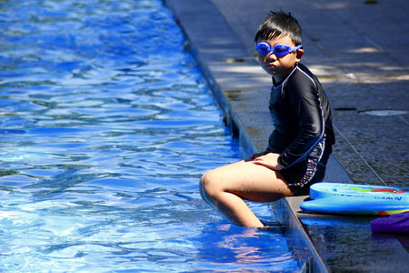 Young kid sitting by the edge of a swimming pool.