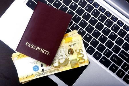 Passport and Philippine peso bills on a laptop computer keyboard.のeditorial素材