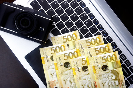 Camera and Philippine peso bills on a laptop computer keyboard.