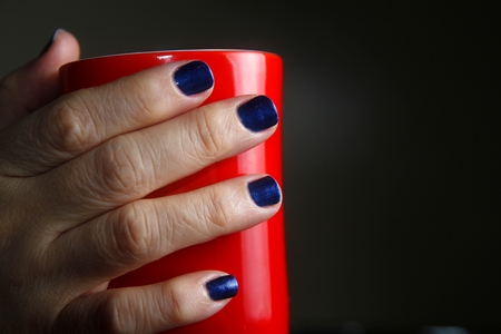 Pair of hands with polished nails holding a red coffee mugの写真素材