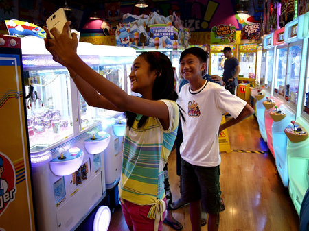 Young kids take a selfie using a smartphone inside an amusement arcade