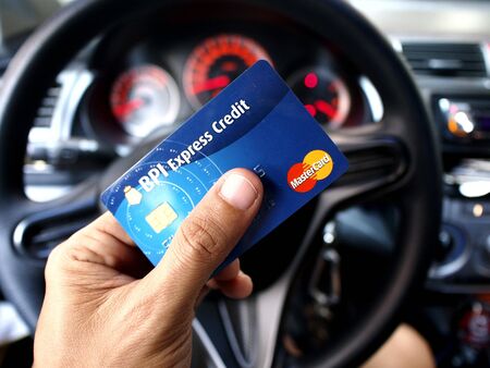 Hand holding a credit card in front of a car's steering wheelの素材