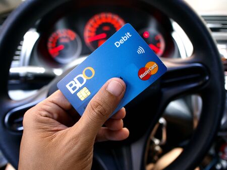 Hand holding a credit card in front of a car's steering wheelの素材