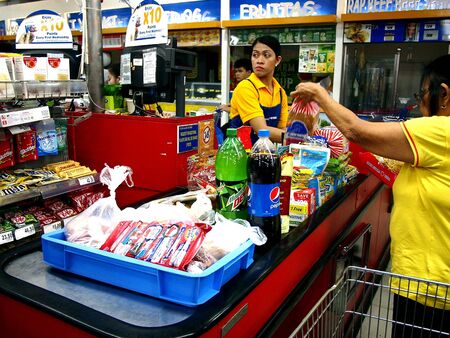 A cashier at a grocery store attends to a customer's grocery itemsの素材