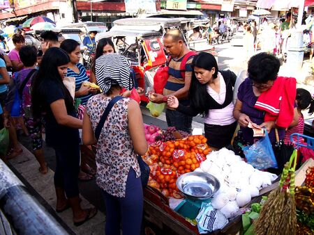 Customers look at assorted fruits and vegetables at a makeshift stall by a sidewalkの素材