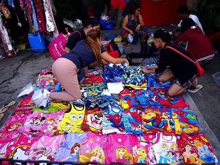 Customers look at assorted shoes and slippers at a makeshift stall by a sidewalkの素材