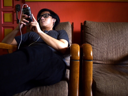 Asian teenager using a smartphone while seated on a couchの写真素材