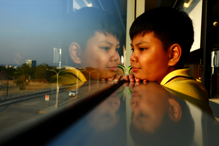 Photo of a young Asian boy looking out a glass windowの写真素材