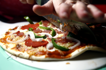 Photo of a ham, pepperoni, cheese with green bell pepper pizza being slicedの写真素材